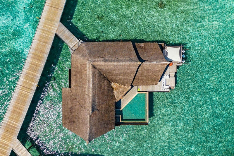 A water villa at OZEN RESERVE Bolifushi seen straight down, its thatched roof and pool set in green water