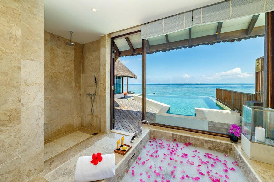 A villa bathroom at OZEN RESERVE Bolifushi, a tub heaped with pink petals opening onto the sea