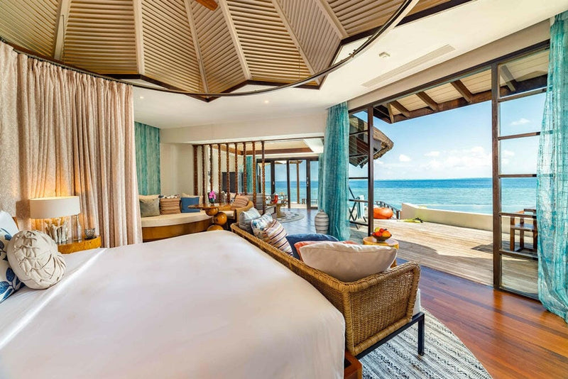A water villa bedroom at OZEN RESERVE Bolifushi, turquoise curtains and a faceted timber slat ceiling