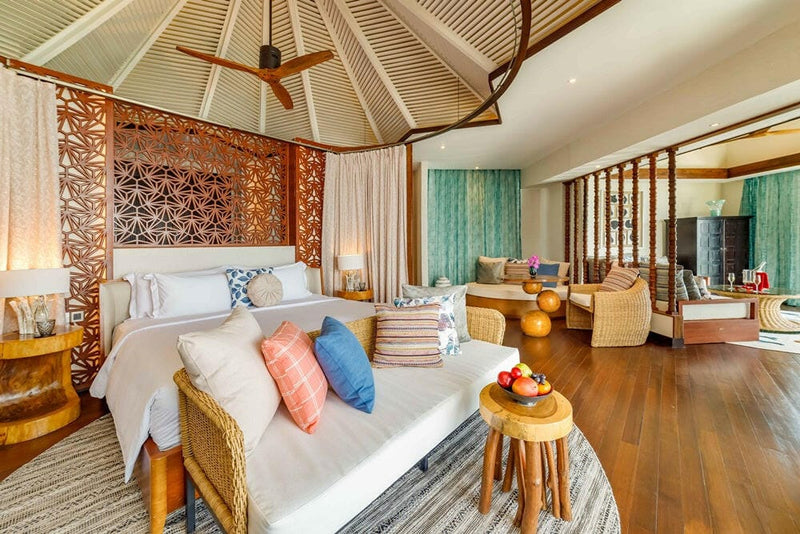 A villa bedroom at OZEN RESERVE Bolifushi, coral and blue cushions against a carved timber headboard wall