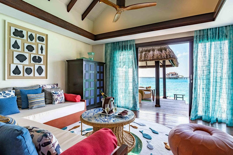 A villa living area at OZEN RESERVE Bolifushi, a champagne bucket on the table and a tan leather pouffe