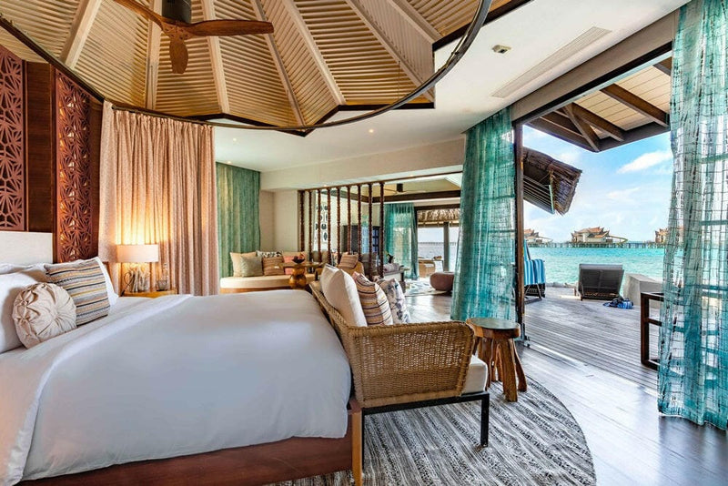 A water villa bedroom at OZEN RESERVE Bolifushi, a carved panel wall and doors open to the lagoon