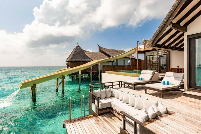 The deck of a water villa at OZEN RESERVE Bolifushi, an L-shaped sofa beside the pool and the slide