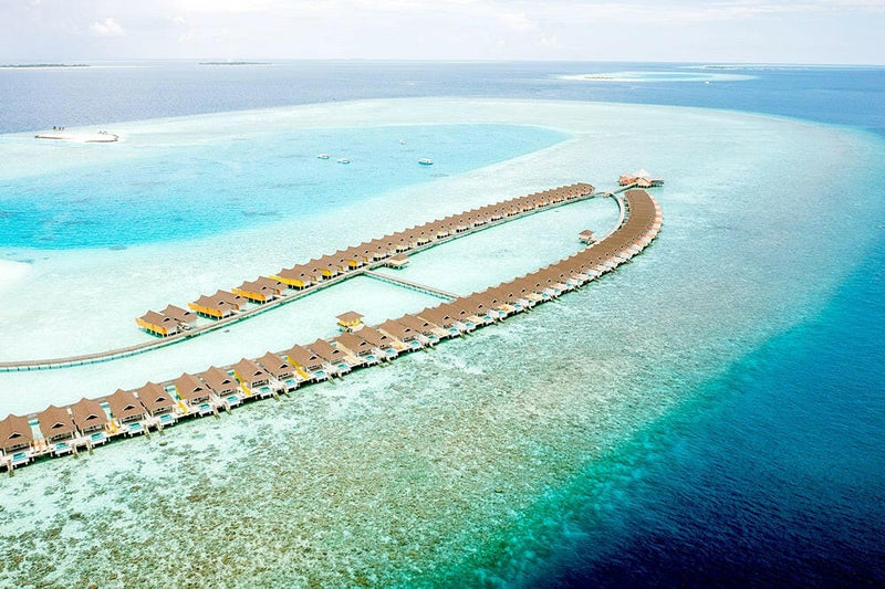 The water villa jetty at The Standard Huruvalhi from the air, curving over the reef into deep blue.