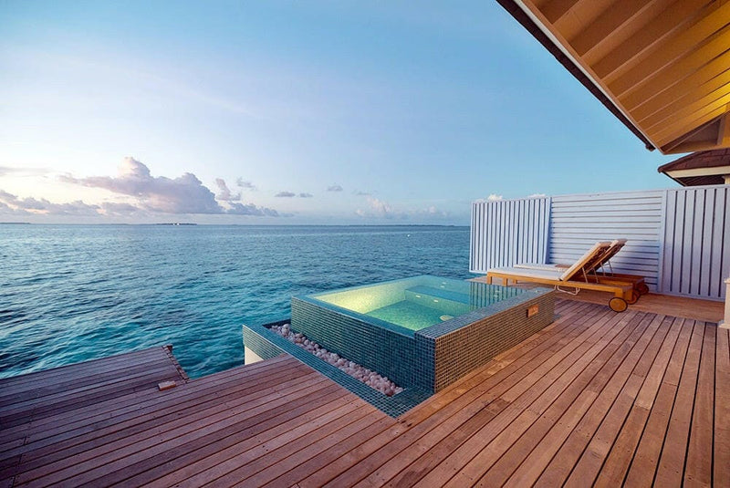 A water villa deck at The Standard Huruvalhi at dusk, a lounger beside a teal edged plunge pool.
