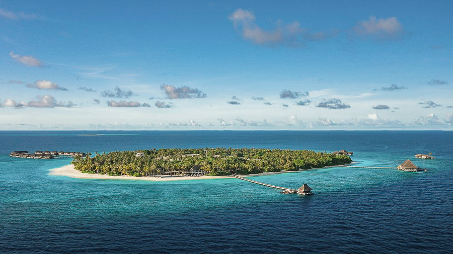An aerial view of Velaa Private Island, its beach and lagoon ringed by open sea.