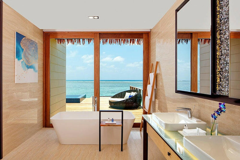 A villa bathroom at Radisson Blu Maldives, freestanding tub facing doors onto the lagoon deck.