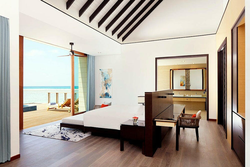 A villa bedroom at Radisson Blu Maldives, dark timber desk and doors onto a deck with loungers.