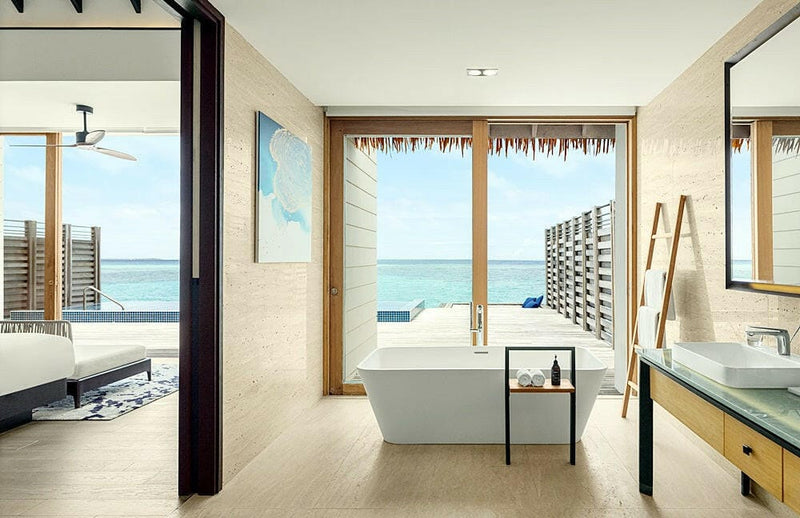 A villa bathroom at Radisson Blu Maldives, tub by louvred windows with the bedroom through the door.