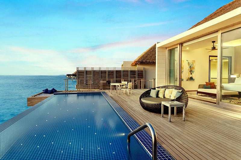 A villa deck at Radisson Blu Maldives at dusk, long blue pool, round daybed and a lit interior.