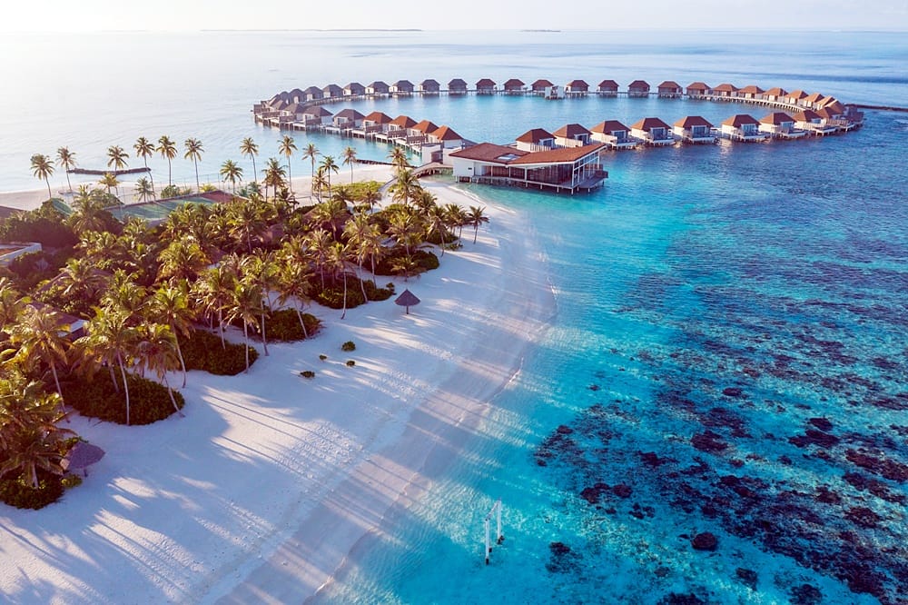 Radisson Blu Resort Maldives at golden hour, overwater villas running along the beach
