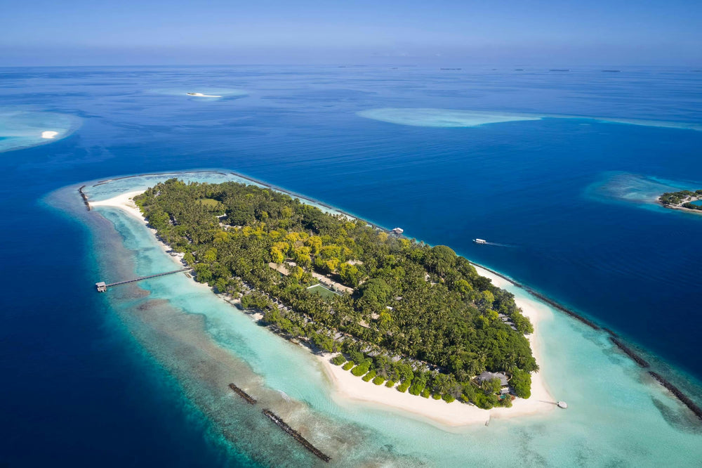 Aerial view of Royal Island Resort in Baa Atoll, the wooded island ringed by its house reef and a pale lagoon