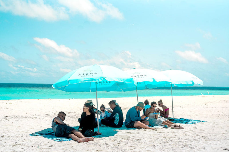 Guests under sun umbrellas on a sandbank trip from Maafushi