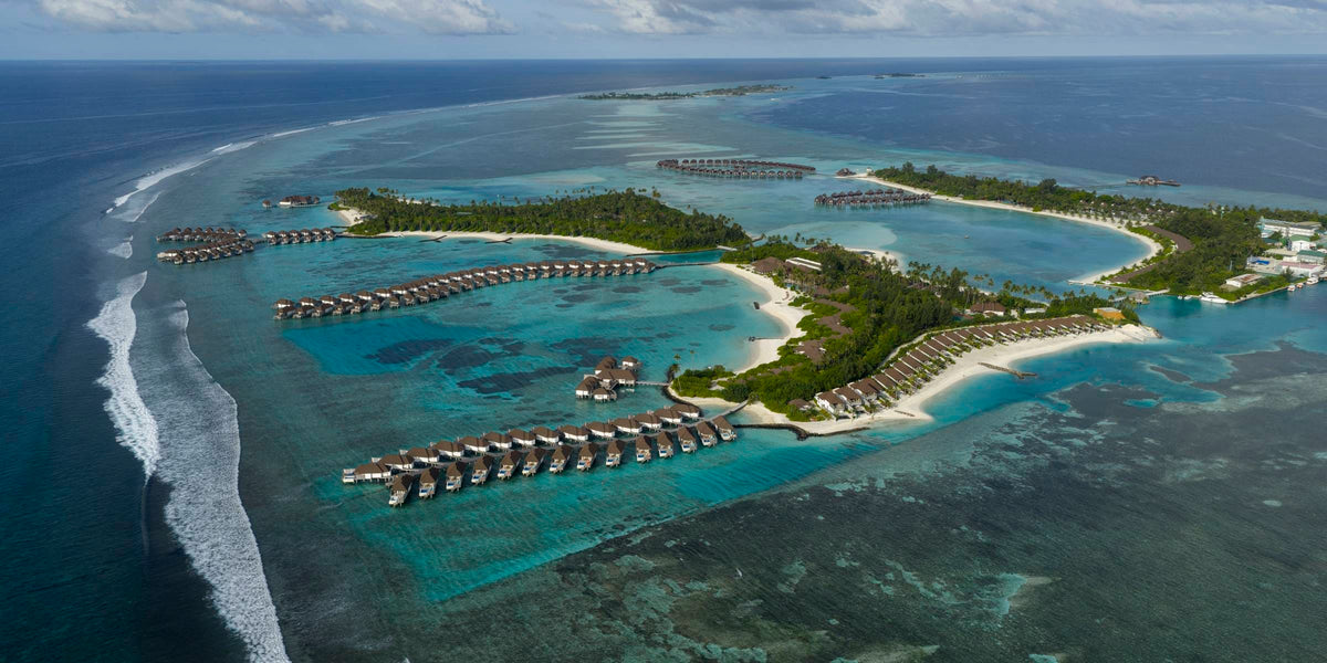 Sun Siyam Olhuveli from the air, surf breaking on the reef edge beside the island and its overwater villas