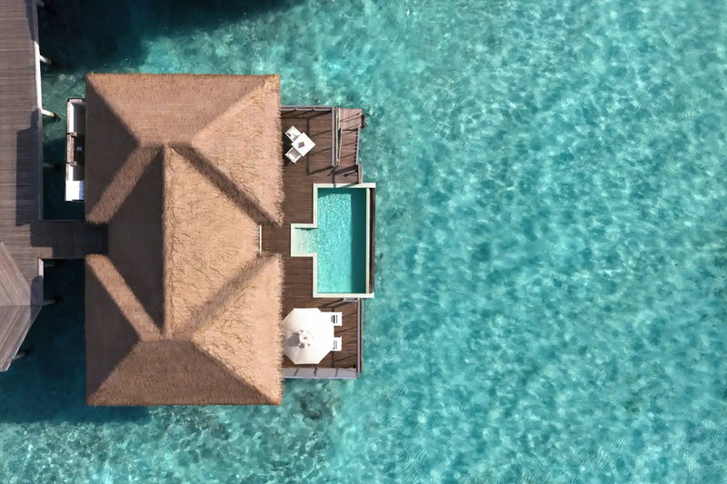 A water villa at Noku Maldives from above, turquoise plunge pool and parasol on the timber deck.