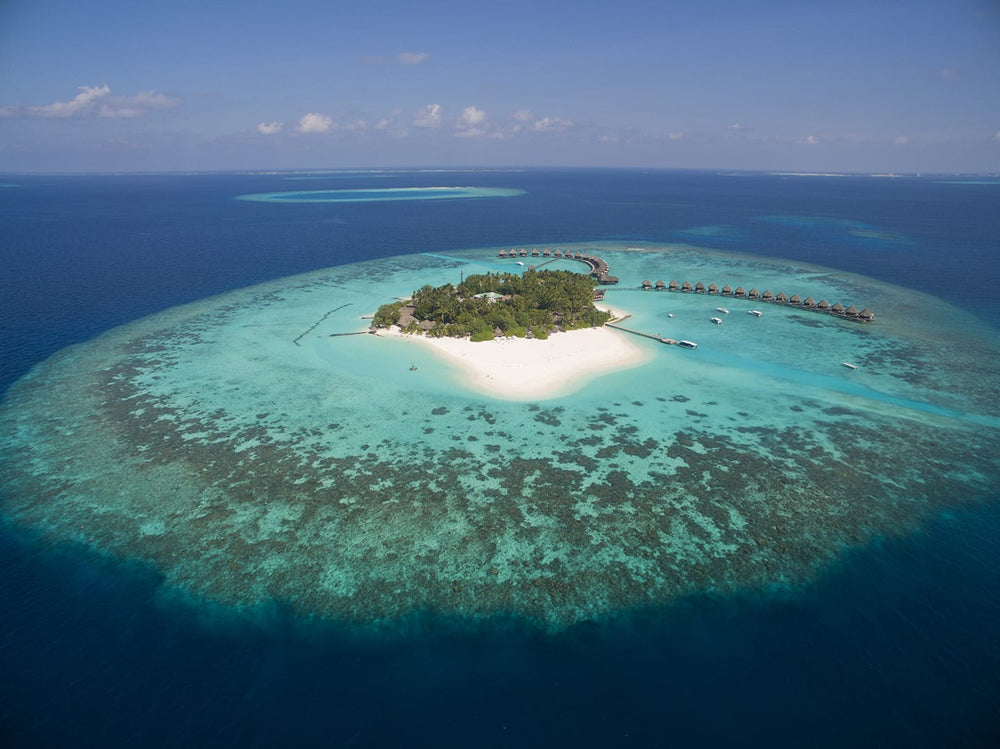Thulhagiri from the air, the small island set in a wide pale lagoon with the reef edge well out from the beach