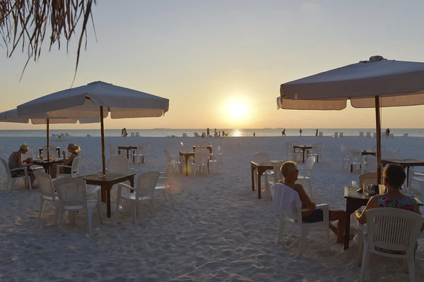 Tables and parasols at the beach bar as the sun sets at Thulhagiri Island Resort