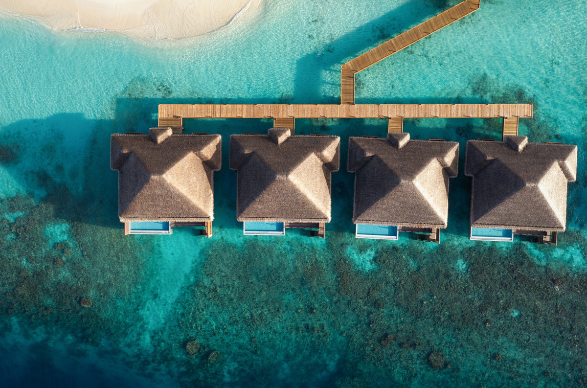 Overwater villas at V Villas Maldives at Mirihi from directly above, thatched roofs and small deck pools along a timber walkway over the reef.