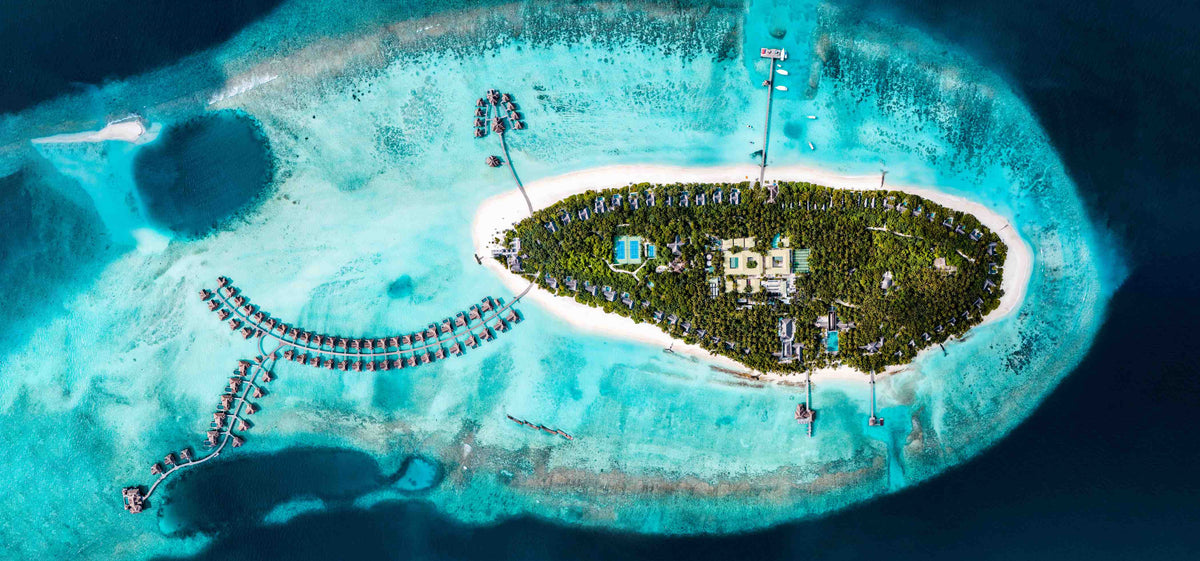 Vakkaru Maldives from the air, the oval island ringed by overwater villas over pale shallow water