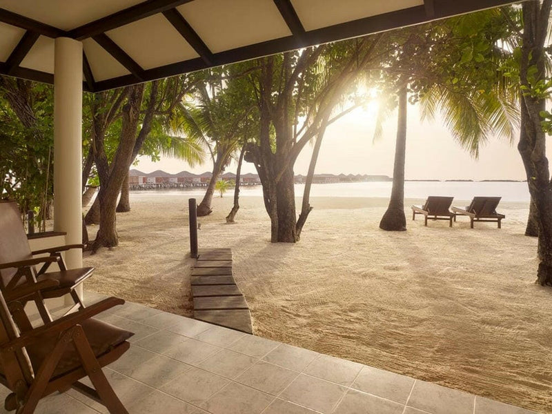 The veranda of a Beach Villa at Villa Nautica, looking through palms to loungers on the sand.