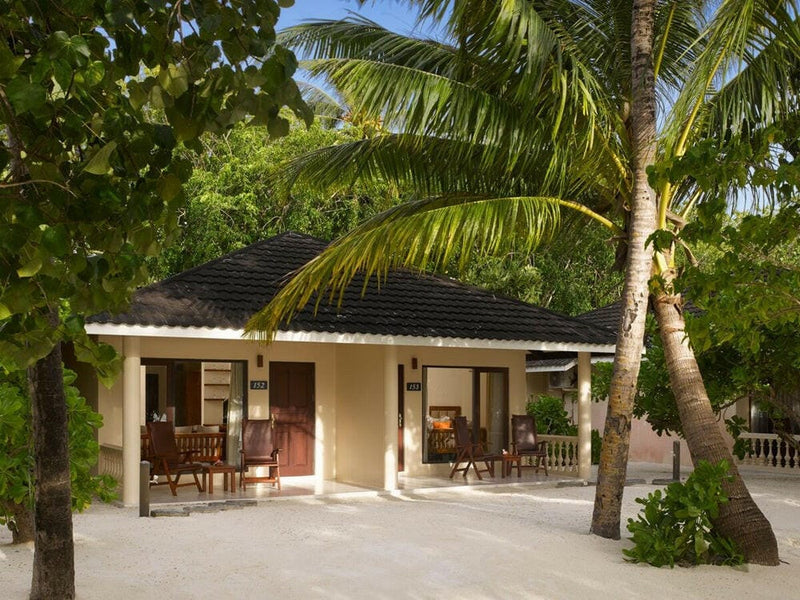 A two bedroom beach villa at Villa Nautica seen from the garden, dark tiled roof under leaning palms.