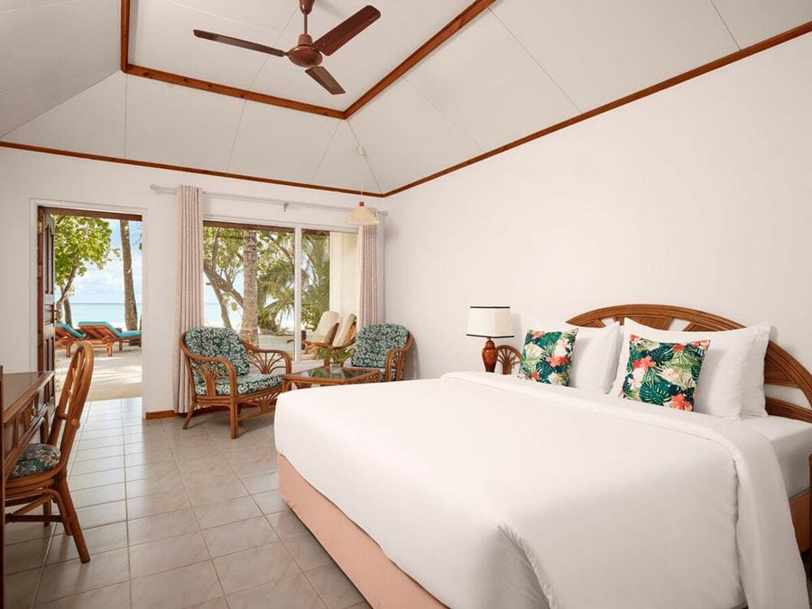 A beach villa bedroom at Villa Park Sun Island, turquoise cushions on white linen under a ceiling fan
