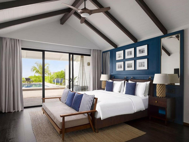 A villa bedroom at Villa Nautica, framed prints above a navy headboard under dark timber beams.