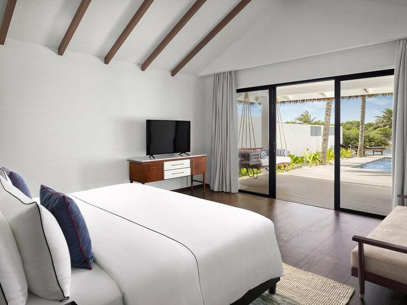 A villa bedroom at Villa Nautica, navy cushions on white linen beneath exposed dark rafters.