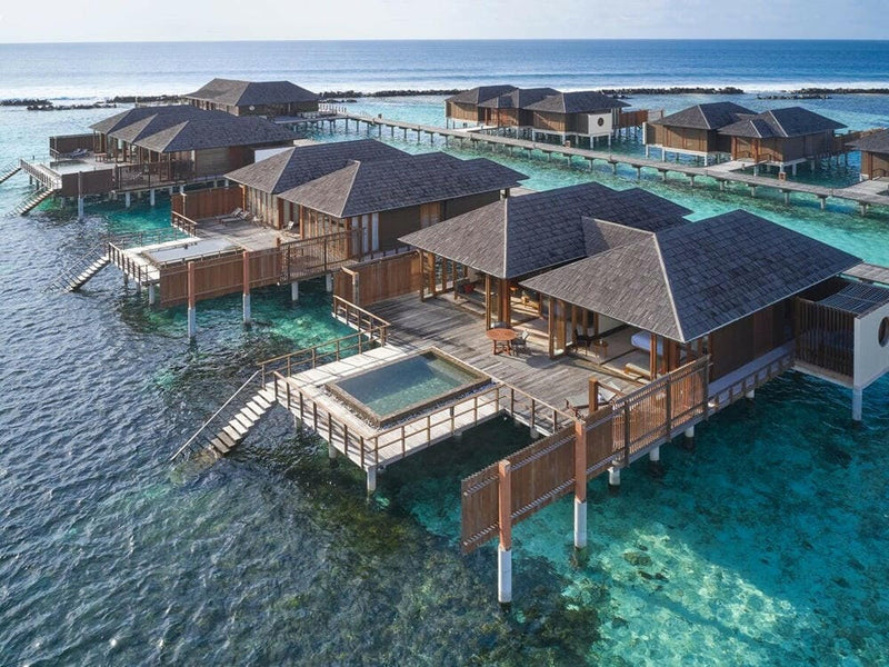 Overwater suites at Villa Nautica from the air, grey roofs and pool decks strung across the reef.