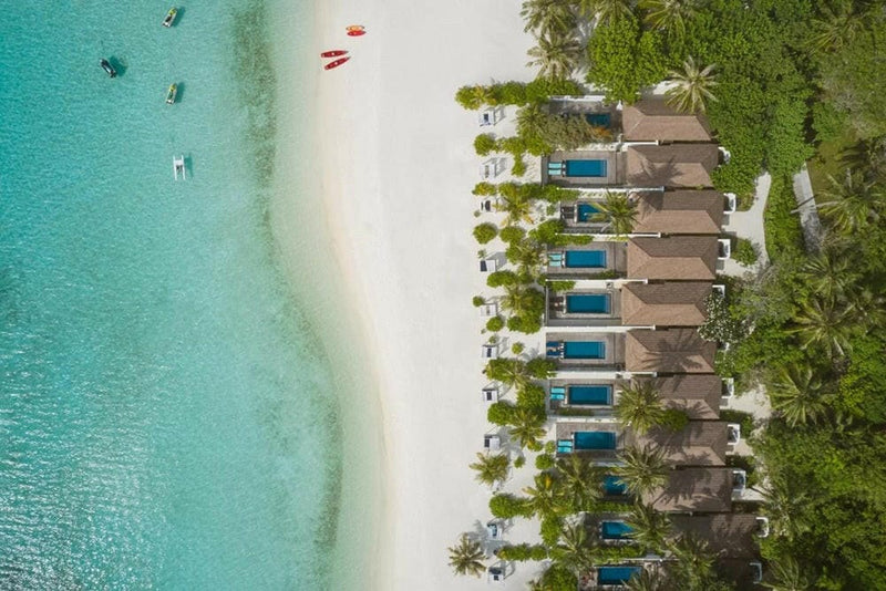 Villa Nautica from the air, a row of beach villas behind palms with the shallows running clear.