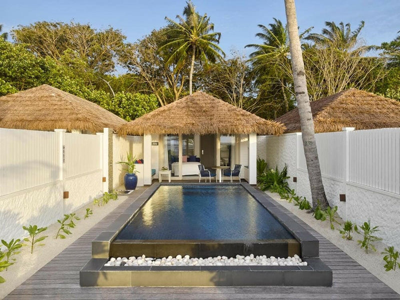 A long private pool at Villa Nautica, walled in white with thatched roofs rising behind the palms.