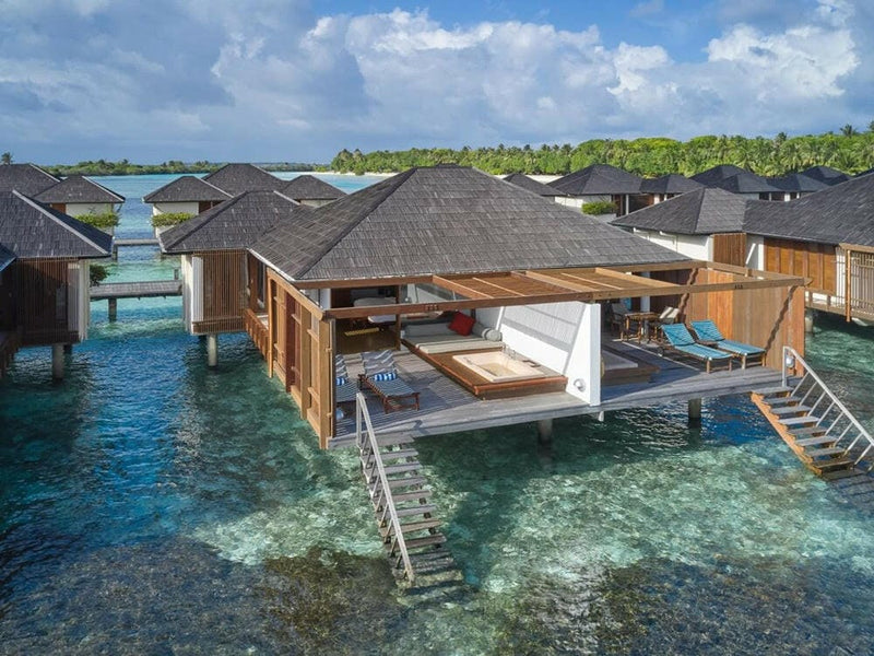 A water villa at Villa Nautica from the air, sun deck and timber ladder dropping into turquoise shallows.