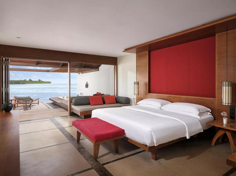 A water villa bedroom at Villa Nautica, twin beds against a deep red panel, doors open to the lagoon.
