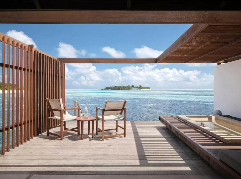 The deck of a water villa at Villa Nautica, two chairs and a sunbed facing a small green island.