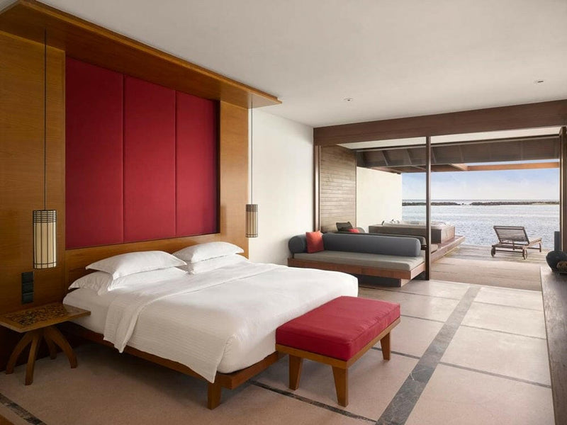 A water villa bedroom at Villa Nautica, twin beds beside a red panel with the deck loungers beyond.
