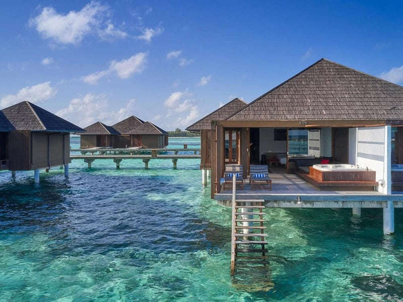 Water villas at Villa Nautica seen from the lagoon, timber steps dropping into clear shallow water.