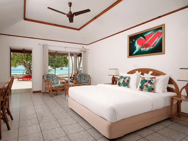 A beach villa bedroom at Villa Park Sun Island, a framed red painting above the bed and cane chairs by the doors