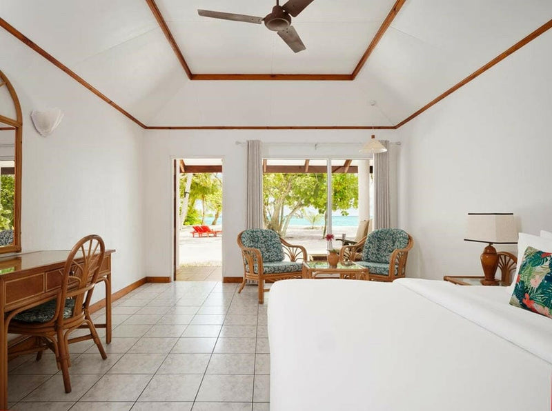 A cane desk beside the bed in a beach villa at Villa Park Sun Island, doors open to the green garden