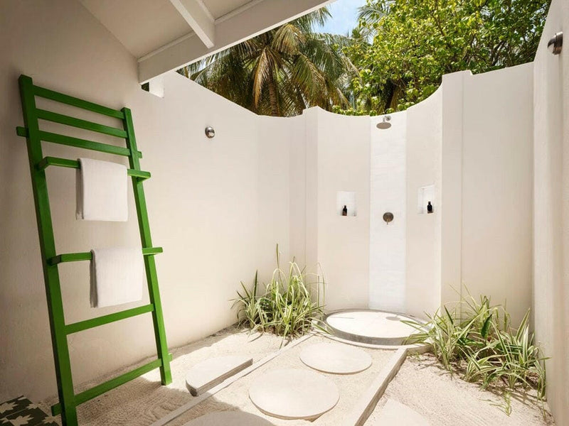 An open-air shower court at Villa Park Sun Island, white walls open to the palms and a green towel ladder