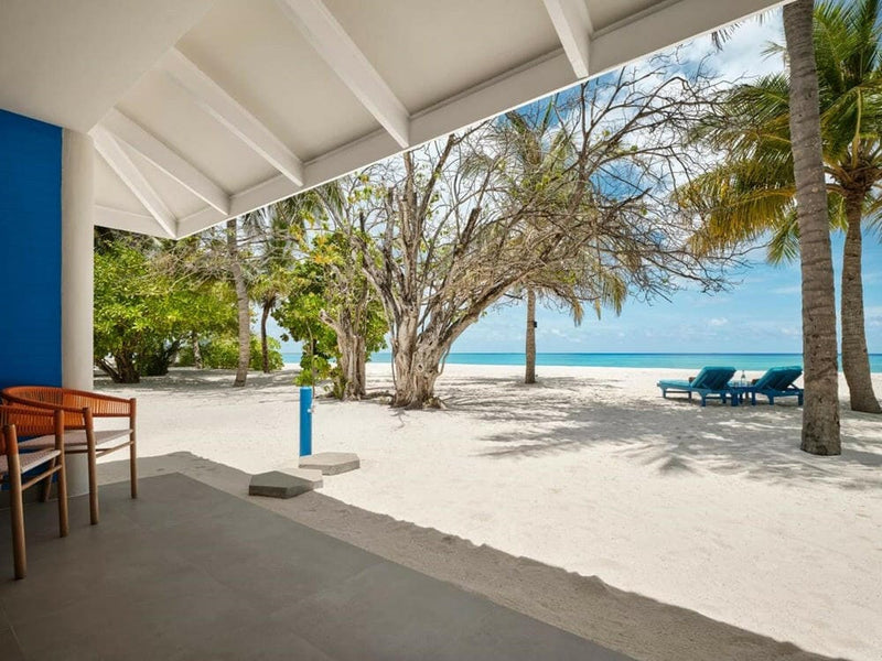 A covered villa terrace at Villa Park Sun Island, timber chairs and an outdoor shower post on the sand