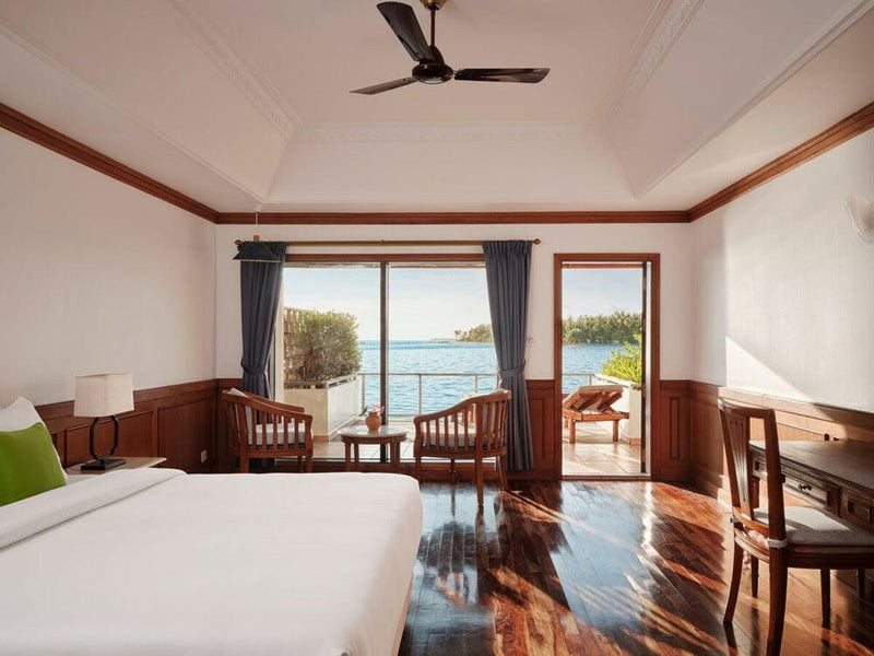 A water villa bedroom at Villa Park Sun Island, balcony doors open to a cane chair and the open sea