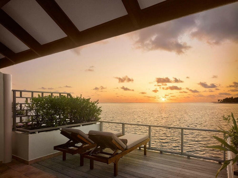 Sunset from a water villa balcony at Villa Park Sun Island, two timber loungers facing the low sun