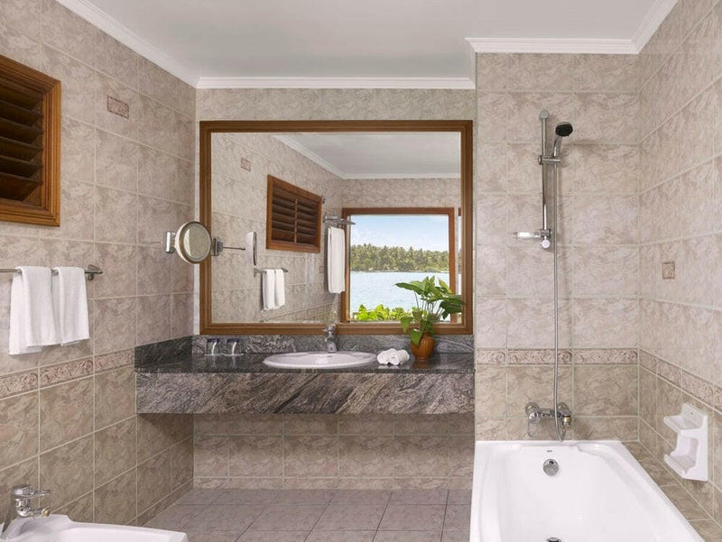 A villa bathroom at Villa Park Sun Island, a granite counter and shaving mirror by a louvred window