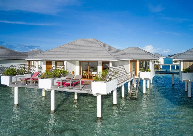 A water villa at Villa Park Sun Island standing on white stilts, red loungers on its deck above the lagoon