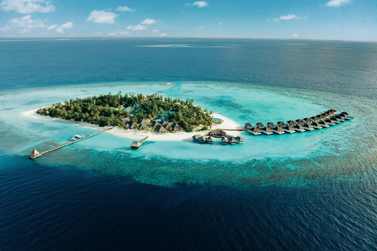 Nova Maldives from the air, a small wooded island with a line of overwater villas off one end