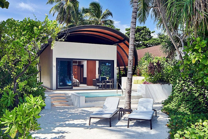 A beach villa at The Westin Maldives Miriandhoo, curved roof, plunge pool and loungers on the sand.