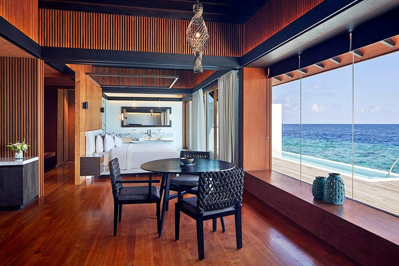 A villa dining table at The Westin Maldives Miriandhoo, woven black chairs under a rattan pendant.