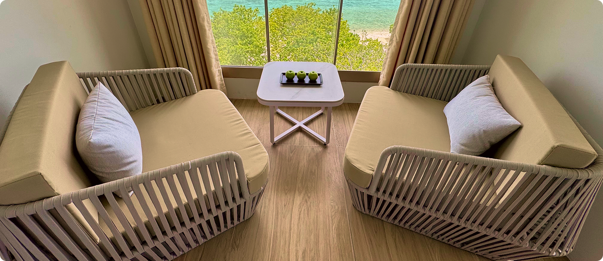 Two armchairs at a full-height window looking over the trees to the sea at Avyanna Gulhi Beach Hotel