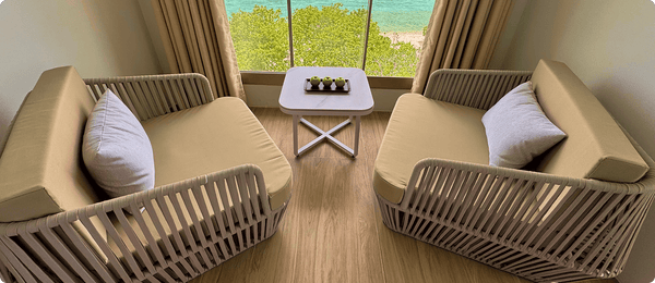 Two armchairs at a full-height window looking over the trees to the sea at Avyanna Gulhi Beach Hotel