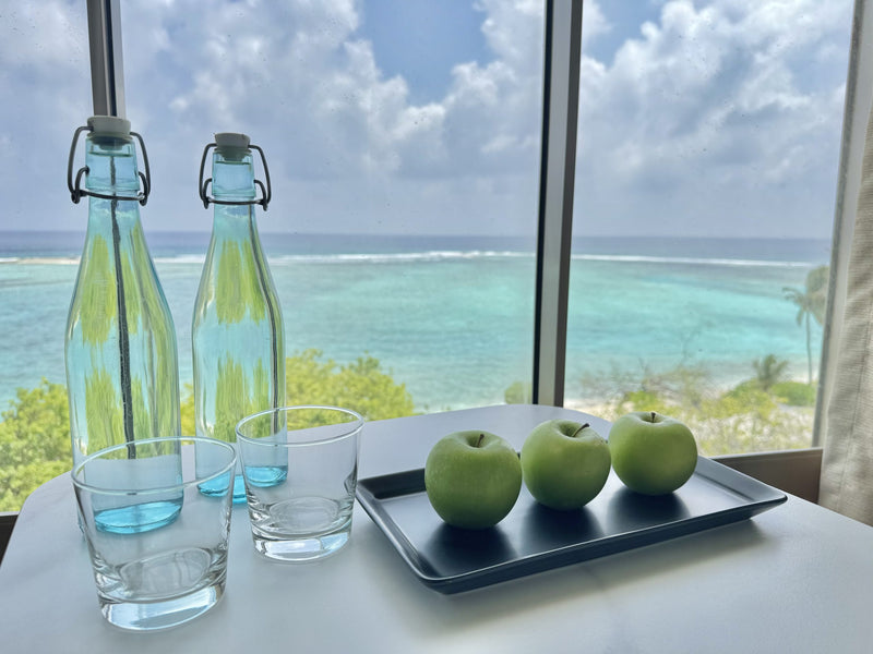Water bottles and green apples on a tray by a window over the Gulhi lagoon